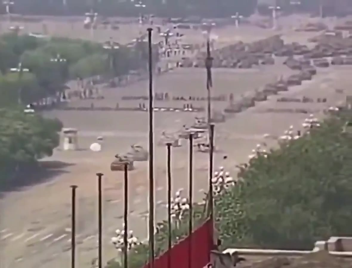 An armoured column stretched across the far end of a wide avenue, seen from a height.